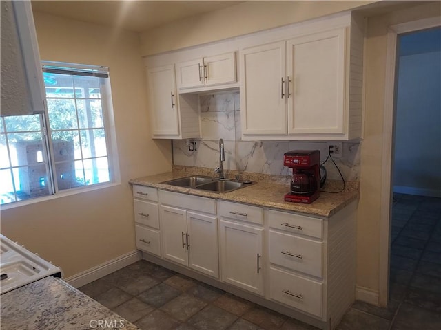 kitchen with decorative backsplash, light stone countertops, baseboards, white cabinetry, and a sink