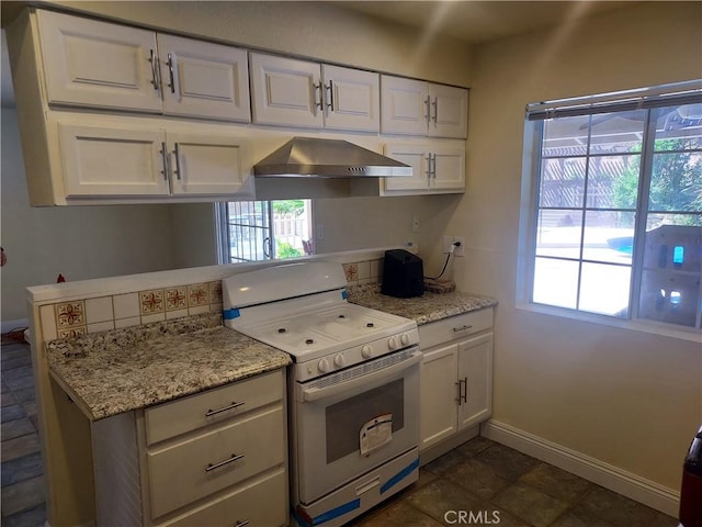 kitchen with light stone countertops, baseboards, white cabinets, white range with gas stovetop, and wall chimney exhaust hood