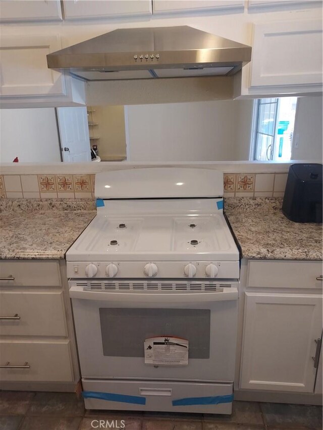 kitchen with light stone counters, white range with gas stovetop, white cabinets, and extractor fan