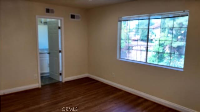 spare room featuring baseboards, visible vents, and wood finished floors