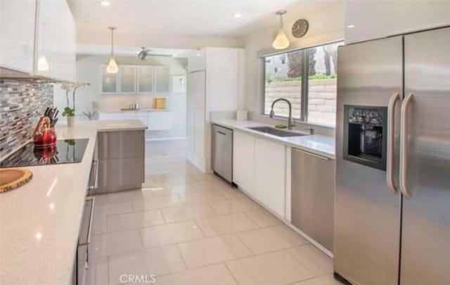 kitchen featuring a sink, decorative backsplash, appliances with stainless steel finishes, white cabinetry, and decorative light fixtures