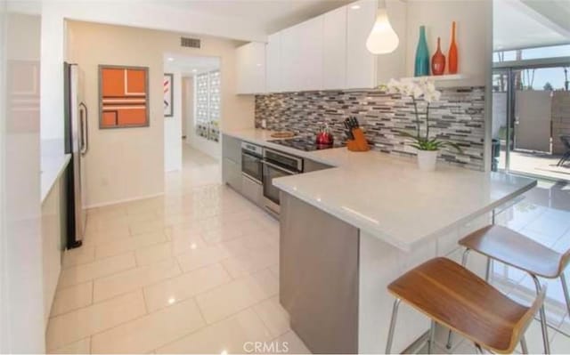 kitchen featuring visible vents, a kitchen bar, a peninsula, white cabinets, and stainless steel appliances