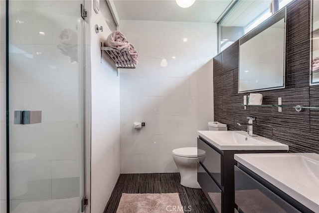 full bath featuring two vanities, a sink, a shower stall, tile walls, and toilet