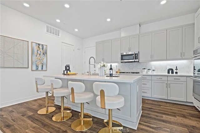 392 Baluster, Irvine, CA 92618 - kitchen with dark wood finished floors, stainless steel microwave, an island with sink, and visible vents