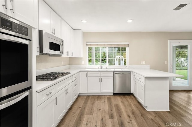 kitchen featuring white cabinets, a peninsula, stainless steel appliances, and light wood-style floors