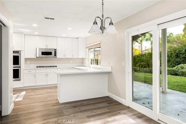 kitchen with white microwave, stovetop, a sink, light countertops, and white cabinets