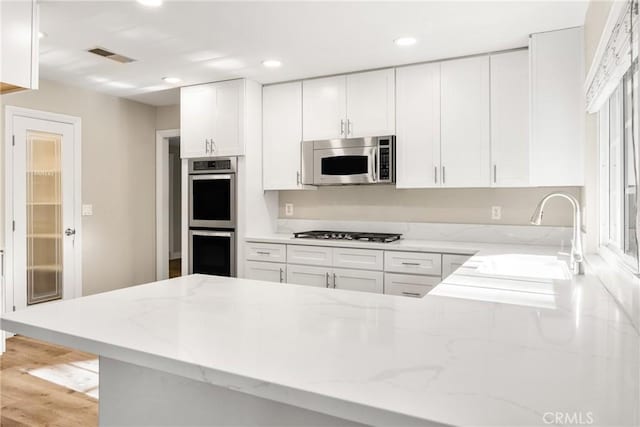 kitchen with visible vents, light stone counters, stainless steel appliances, white cabinetry, and a sink