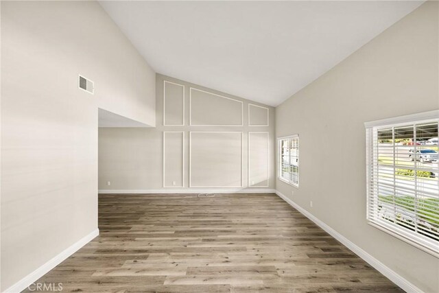 spare room featuring visible vents, baseboards, high vaulted ceiling, and wood finished floors