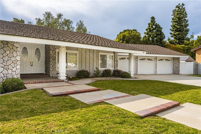 view of front of house with a front yard, concrete driveway, a garage, stone siding, and board and batten siding