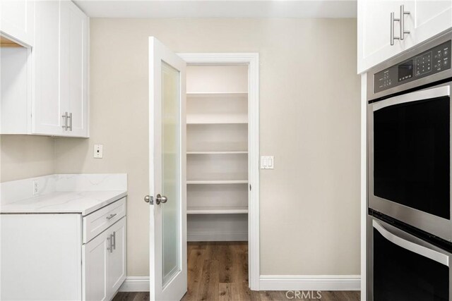 kitchen featuring light stone countertops, baseboards, white cabinets, double oven, and light wood-type flooring