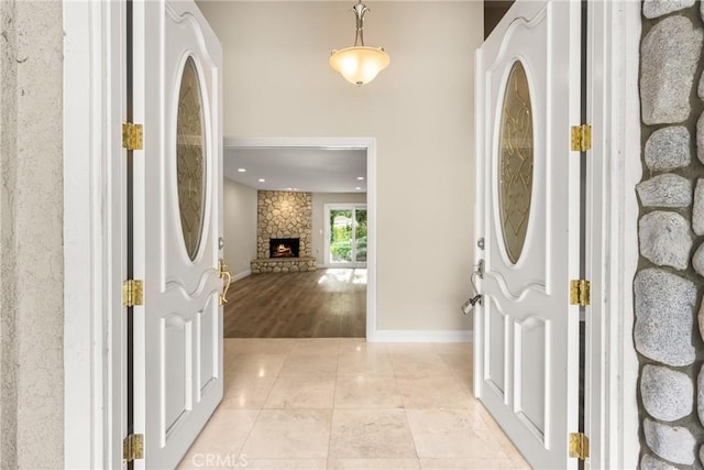 foyer with a stone fireplace, light tile patterned floors, and baseboards