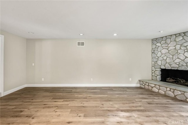 below grade area with visible vents, a stone fireplace, baseboards, and wood finished floors