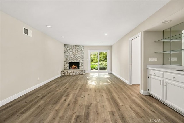 unfurnished living room with light wood finished floors, visible vents, a stone fireplace, and baseboards