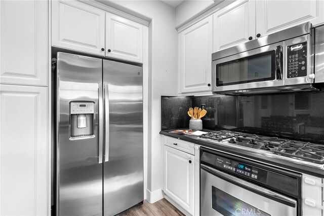 kitchen featuring dark countertops, backsplash, appliances with stainless steel finishes, and white cabinets