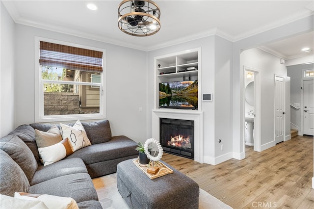 living area with built in features, light wood-style floors, a glass covered fireplace, and ornamental molding