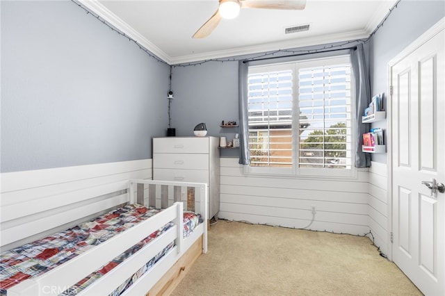 carpeted bedroom with visible vents, a nursery area, wood walls, wainscoting, and crown molding