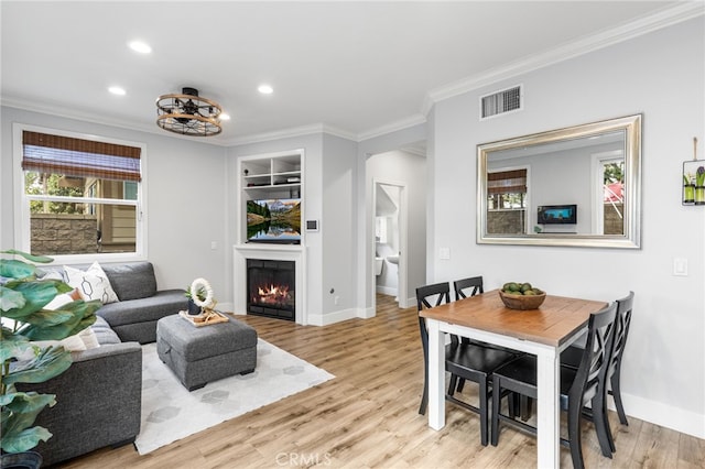 dining space with built in shelves, baseboards, visible vents, light wood finished floors, and crown molding