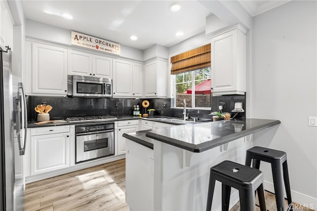 kitchen with white cabinetry, a peninsula, appliances with stainless steel finishes, and a sink