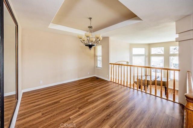 unfurnished room featuring baseboards, a raised ceiling, a notable chandelier, and wood finished floors