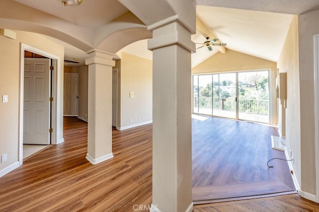 interior space featuring wood finished floors, a ceiling fan, baseboards, ornate columns, and lofted ceiling