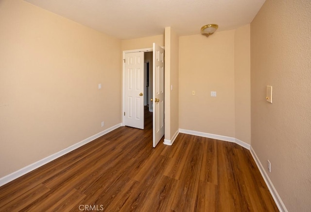 unfurnished room featuring baseboards and dark wood finished floors