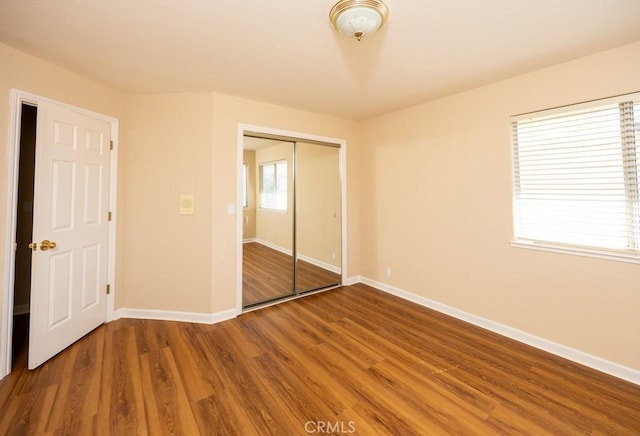 unfurnished bedroom featuring wood finished floors, baseboards, and a closet