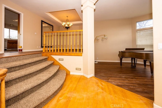 stairway featuring decorative columns, baseboards, an inviting chandelier, and wood finished floors