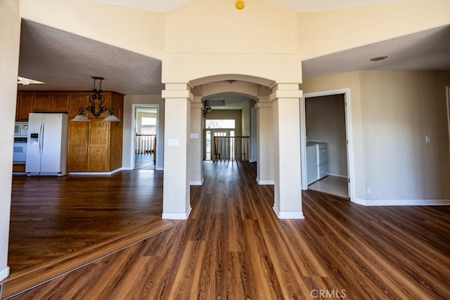 interior space with baseboards, decorative columns, arched walkways, dark wood-type flooring, and washing machine and dryer