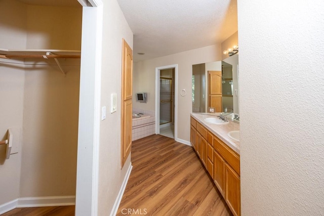 bathroom with a walk in closet, baseboards, double vanity, wood finished floors, and a sink