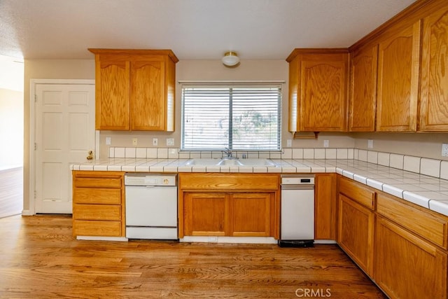 kitchen with brown cabinetry, dishwasher, light wood-style floors, and a sink