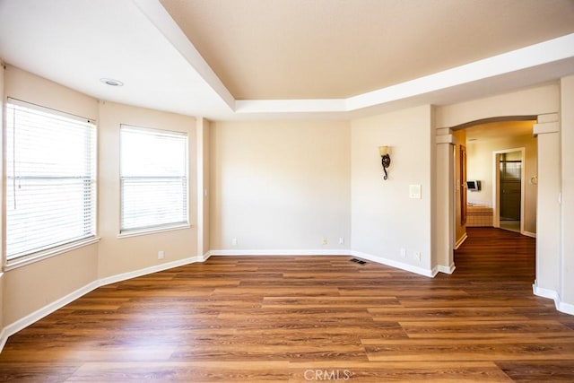 spare room featuring wood finished floors, visible vents, baseboards, arched walkways, and a raised ceiling