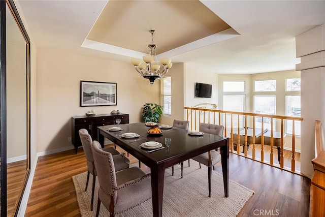 dining space with a raised ceiling, a notable chandelier, wood finished floors, and baseboards