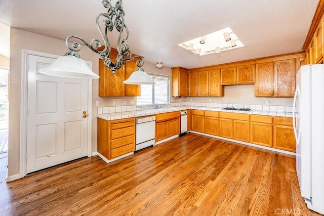 kitchen featuring tile countertops, white appliances, a skylight, and brown cabinetry