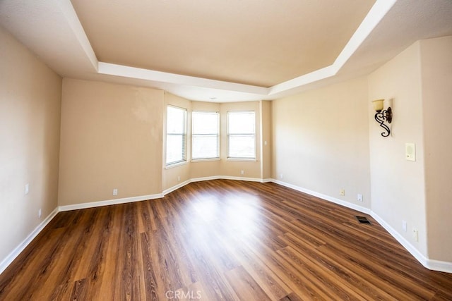 empty room with visible vents, a raised ceiling, baseboards, and dark wood-style floors