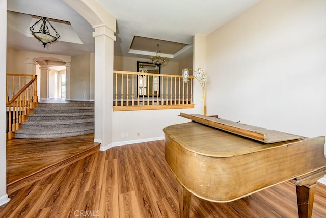 bar with stairway, wood finished floors, baseboards, ornate columns, and a tray ceiling