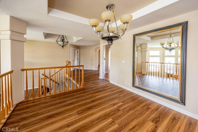 interior space with a tray ceiling, an upstairs landing, an inviting chandelier, and wood finished floors