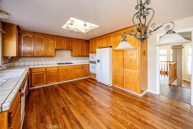 kitchen featuring white appliances, tile counters, brown cabinets, and a sink