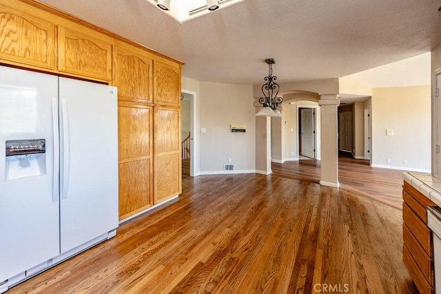 kitchen featuring wood finished floors, visible vents, ornate columns, baseboards, and white refrigerator with ice dispenser