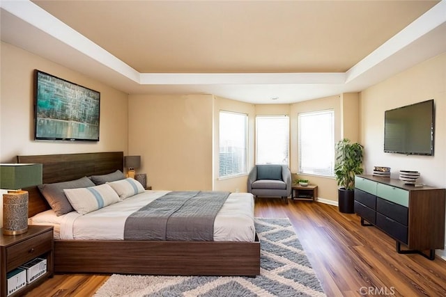 bedroom featuring baseboards, a tray ceiling, and wood finished floors