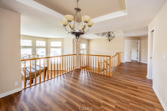 hall with an upstairs landing, a raised ceiling, wood finished floors, an inviting chandelier, and baseboards