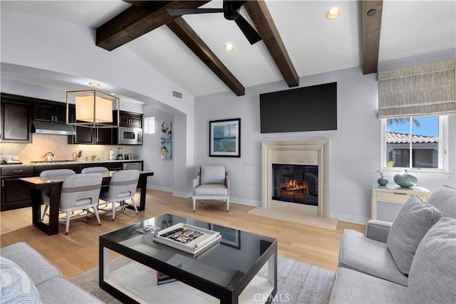 living room with a glass covered fireplace, lofted ceiling with beams, light wood-type flooring, and baseboards