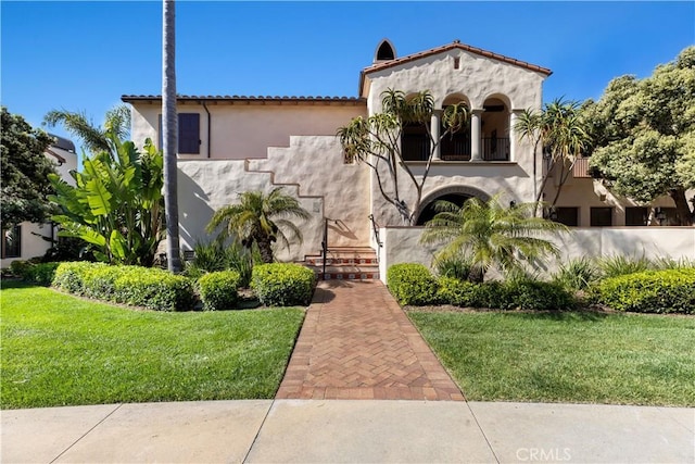 mediterranean / spanish house featuring a tiled roof, a front yard, a balcony, and stucco siding