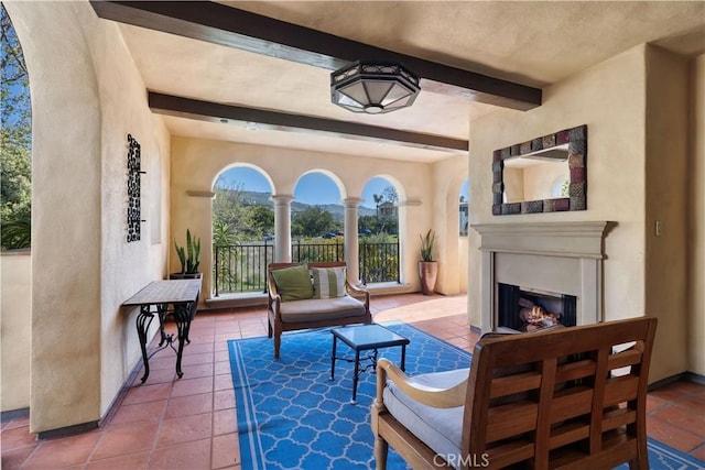 living area featuring beam ceiling, baseboards, tile patterned floors, and a lit fireplace