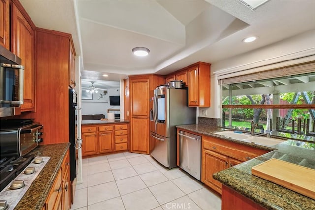 kitchen featuring a tray ceiling, brown cabinets, appliances with stainless steel finishes, and ceiling fan