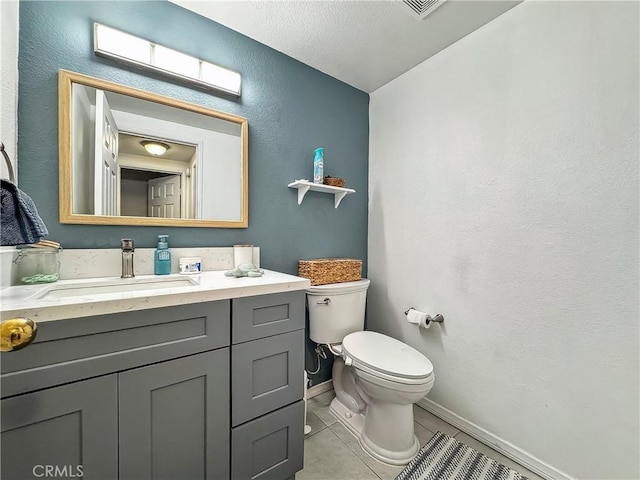 bathroom featuring toilet, tile patterned flooring, baseboards, vanity, and a textured wall