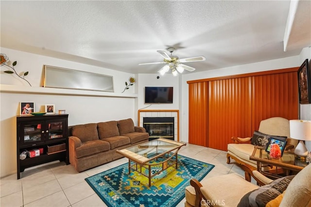 living room featuring a fireplace, light tile patterned flooring, a ceiling fan, and a textured ceiling