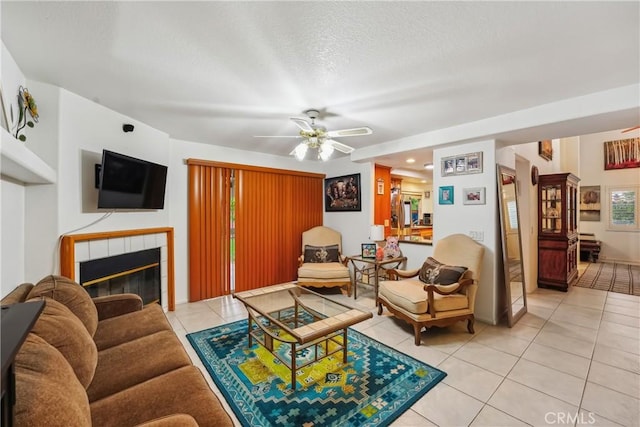 living room featuring light tile patterned floors, a tile fireplace, a textured ceiling, and ceiling fan