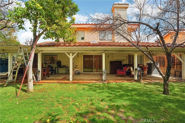 rear view of property featuring a chimney, a lawn, a tile roof, and a patio