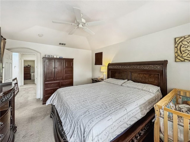 bedroom featuring visible vents, light colored carpet, vaulted ceiling, arched walkways, and a ceiling fan