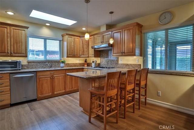 kitchen featuring a skylight, a toaster, a sink, under cabinet range hood, and dishwasher